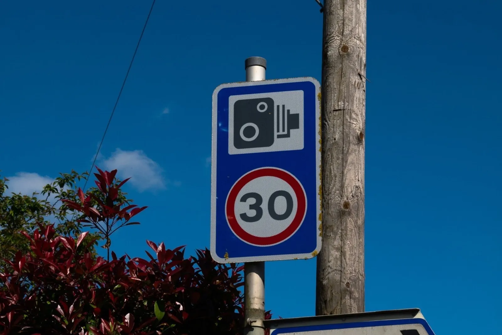 A speed camera sign above a 30 mph roundel against a blue sky