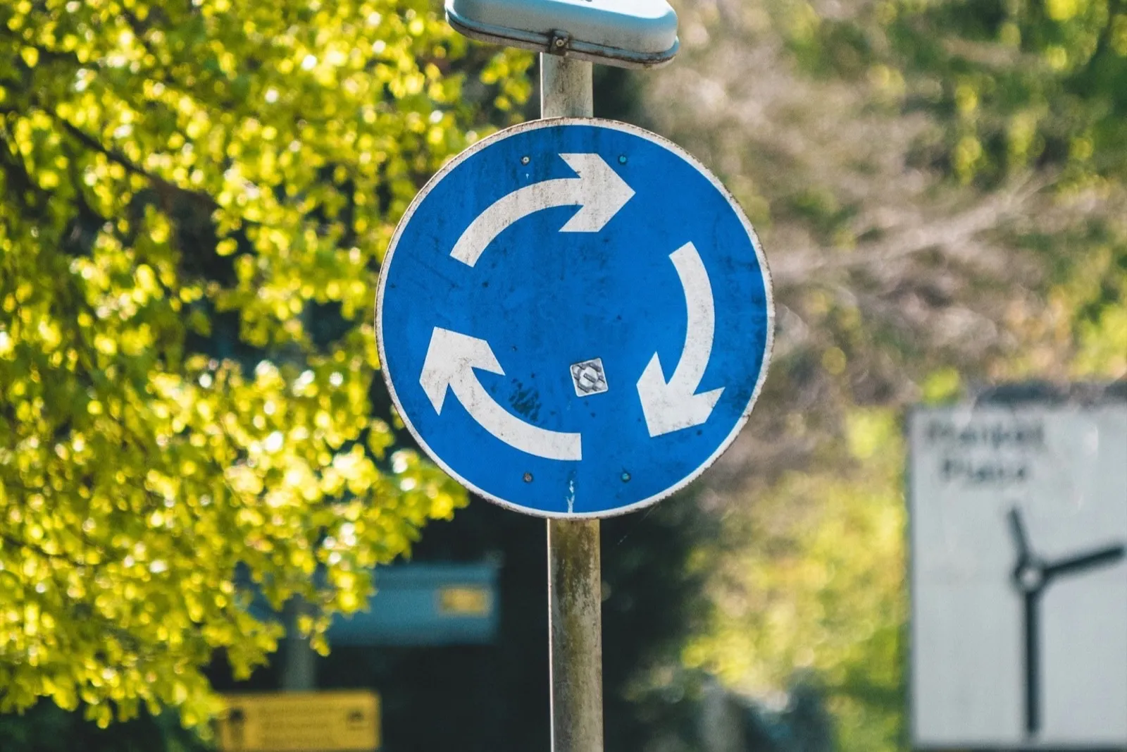 Blue mini-roundabout sign with three white arrows on a pole