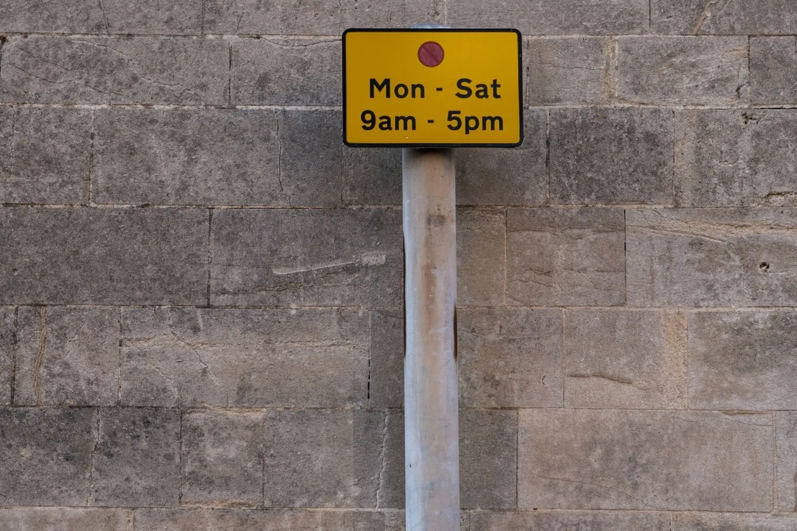 A yellow no-waiting time plate reading Mon-Sat 9am-5pm on a stone wall
