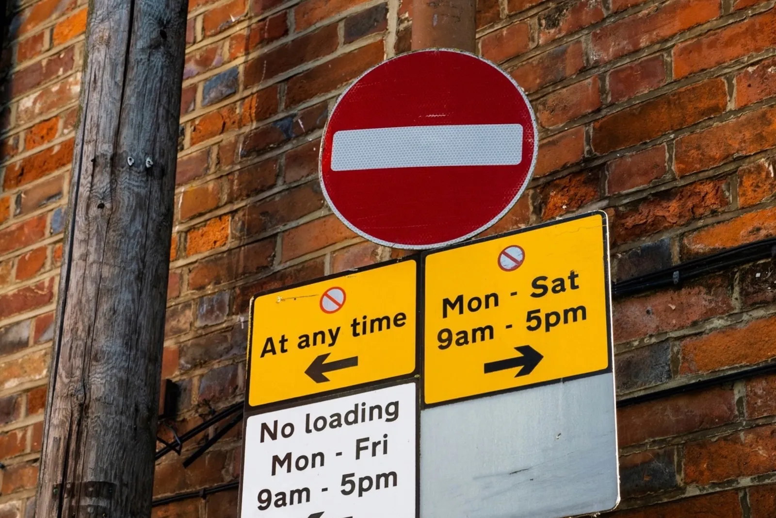 A pole carrying a no-entry sign with 'At any time', 'Mon-Sat 9am-5pm' and 'No loading Mon-Fri 9am-5pm' plates with arrows
